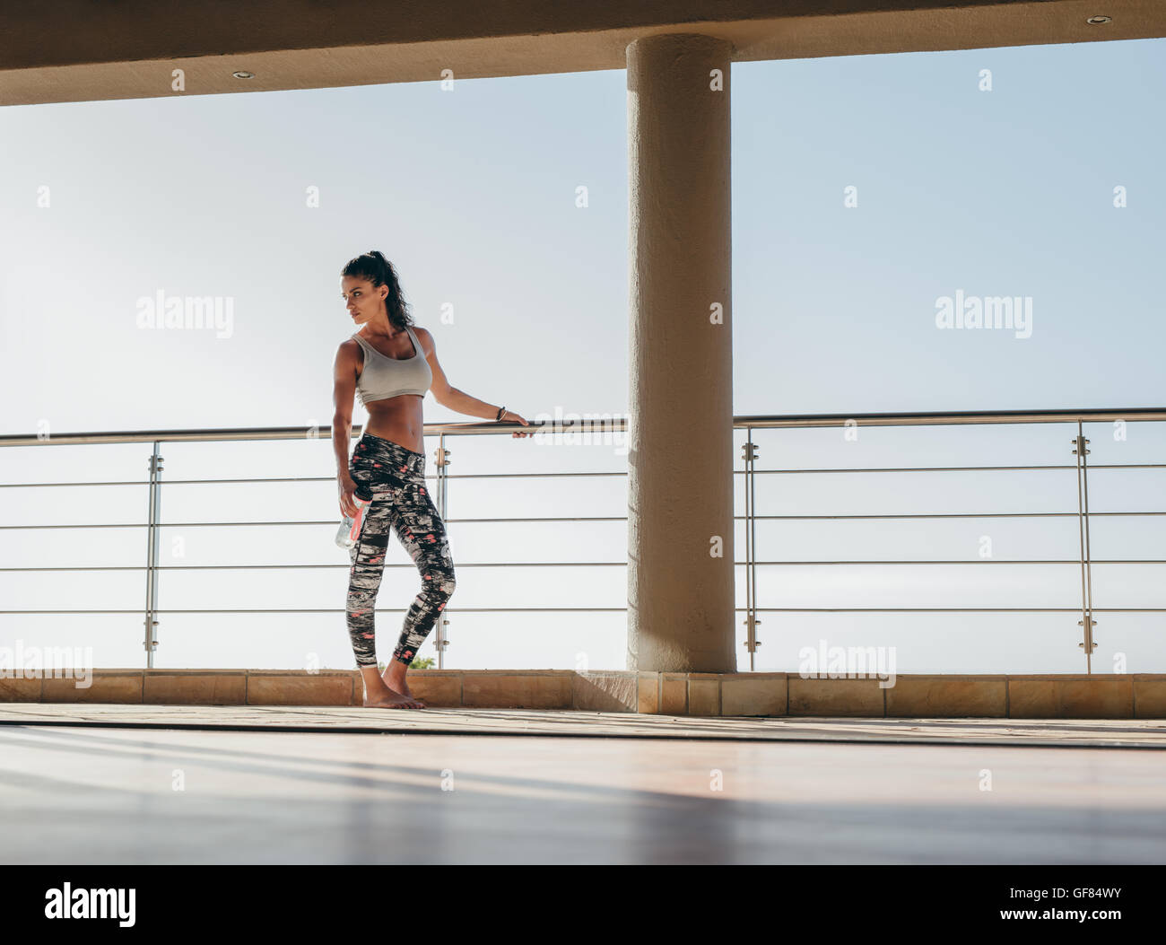 Plan complet de jeune femme en forme debout sur le balcon avec une bouteille d'eau. femme de fitness prenant une pause de l'exercice. Banque D'Images
