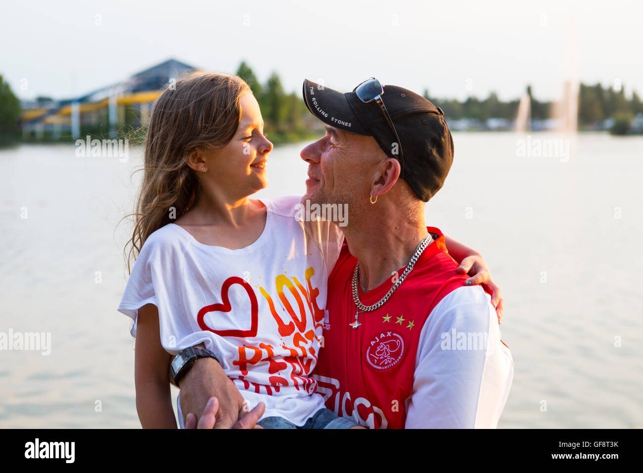 Père tenant sa fille en face d'un lac juste avant le coucher du soleil en été Banque D'Images