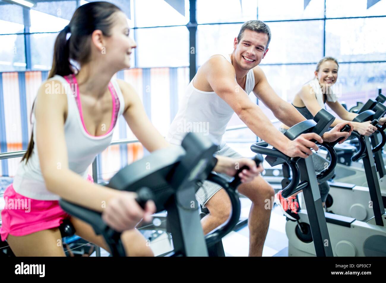 Parution de la propriété. Parution du modèle. Les jeunes hommes et femmes qui travaillent sur des machines d'exercice dans la salle de sport, de sourire. Banque D'Images