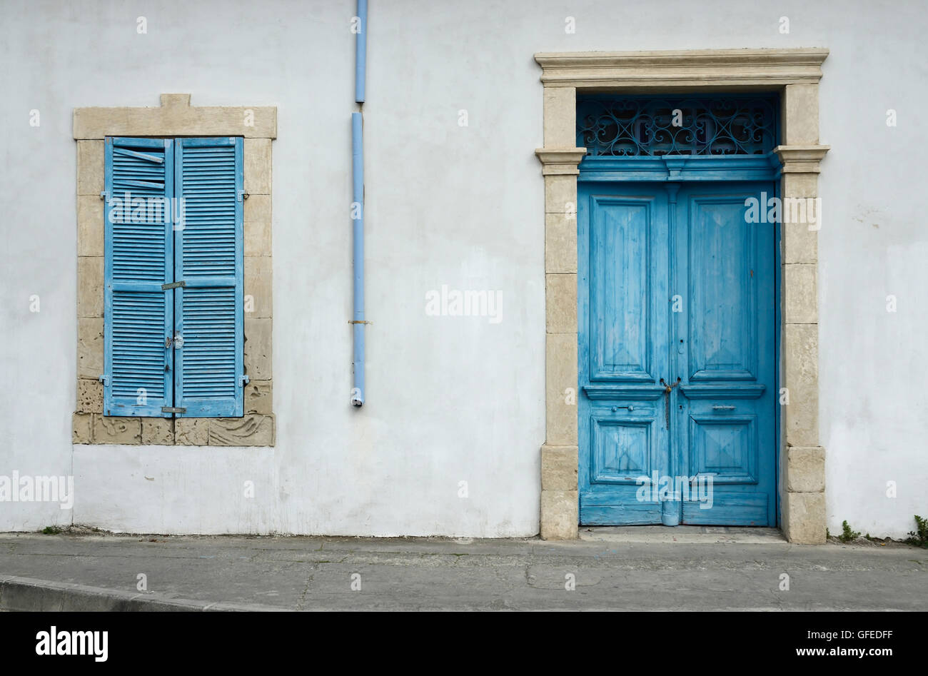 Photo de vieux chypriote typique de bâtiment blanc avec porte en bois bleu vif ,fenêtre avec des volets fermés et tuyau d'eau de pluie Banque D'Images