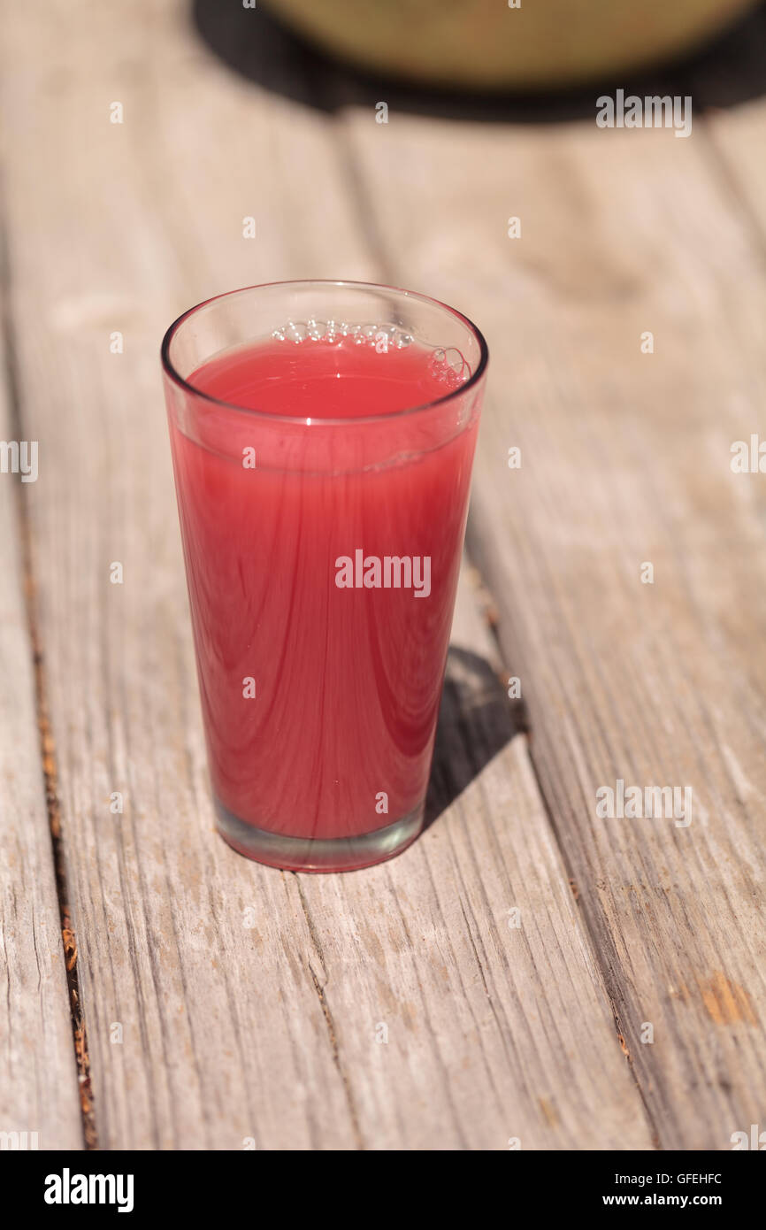 Verre de rose pastèque rouge verre de jus de fruits en été sur une table de pique-nique rustique. Banque D'Images