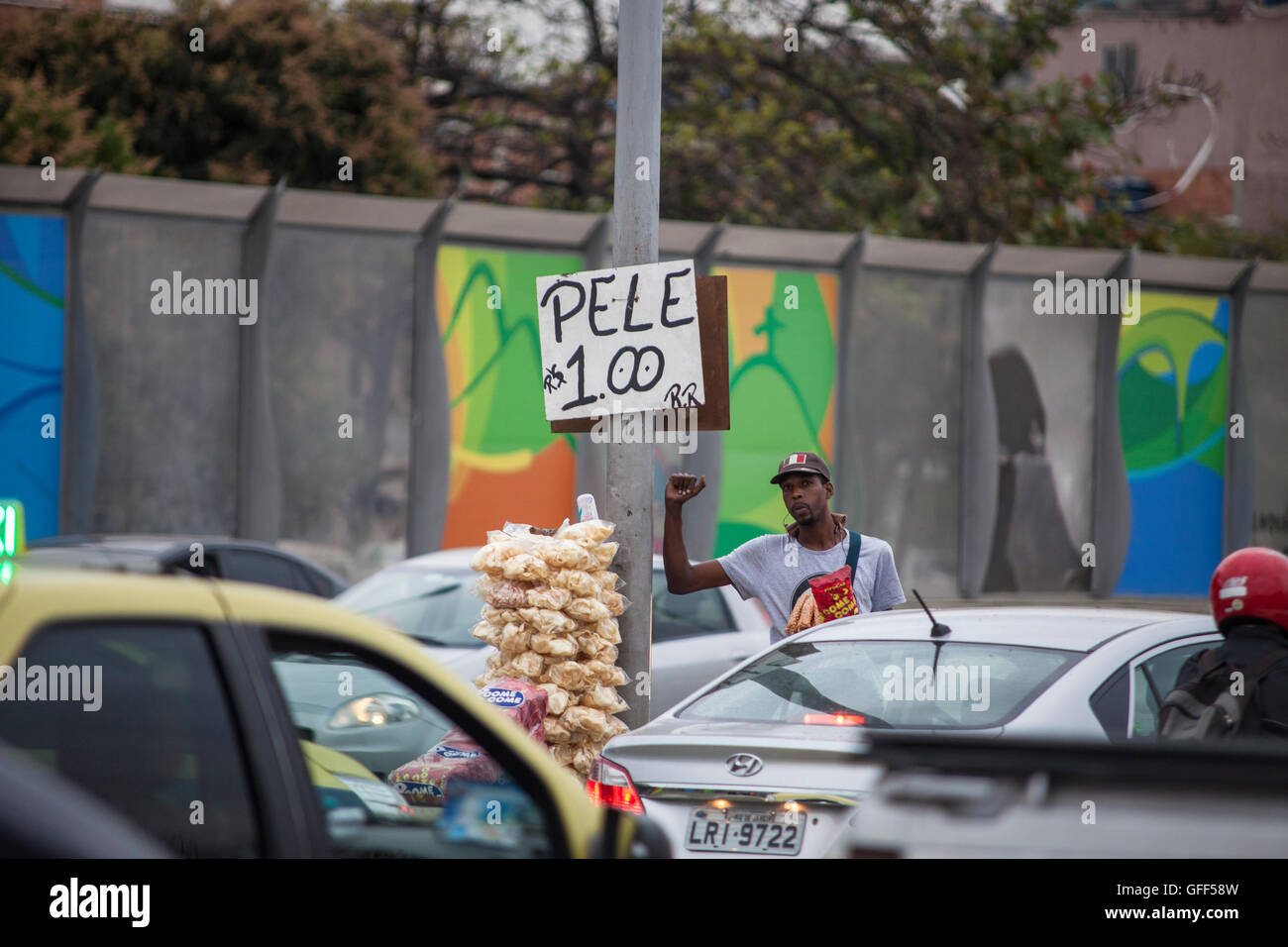 Habitants de Complexo da Mare, un immense réseau de favelas qui siège aux côtés de la Linha Vermelha ( ligne rouge ), la route principale de l'aéroport international de Rio de Janeiro au centre-ville, à travailler comme vendeurs de rue pendant les heures de pointe à l'expreessway - depuis 2010, la communauté a été clôturé à partir de l'autoroute par d'immenses panneaux Perspex - les autorités affirment qu'ils fournissent une barrière acoustique, les sections locales le décrivent comme un "mur de la honte", une autre façon de cacher les pauvres. Juste avant les Jeux Olympiques, la ville a commencé à plâtrer l 3 m de haut, 7 km de panneaux avec des affiches olympiques s Banque D'Images