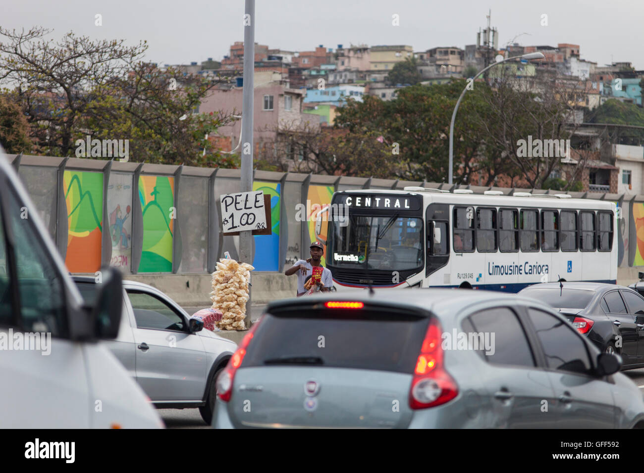 Habitants de Complexo da Mare, un immense réseau de favelas qui siège aux côtés de la Linha Vermelha ( ligne rouge ), la route principale de l'aéroport international de Rio de Janeiro au centre-ville, à travailler comme vendeurs de rue pendant les heures de pointe à l'expreessway - depuis 2010, la communauté a été clôturé à partir de l'autoroute par d'immenses panneaux Perspex - les autorités affirment qu'ils fournissent une barrière acoustique, les sections locales le décrivent comme un "mur de la honte", une autre façon de cacher les pauvres. Juste avant les Jeux Olympiques, la ville a commencé à plâtrer l 3 m de haut, 7 km de panneaux avec des affiches olympiques s Banque D'Images