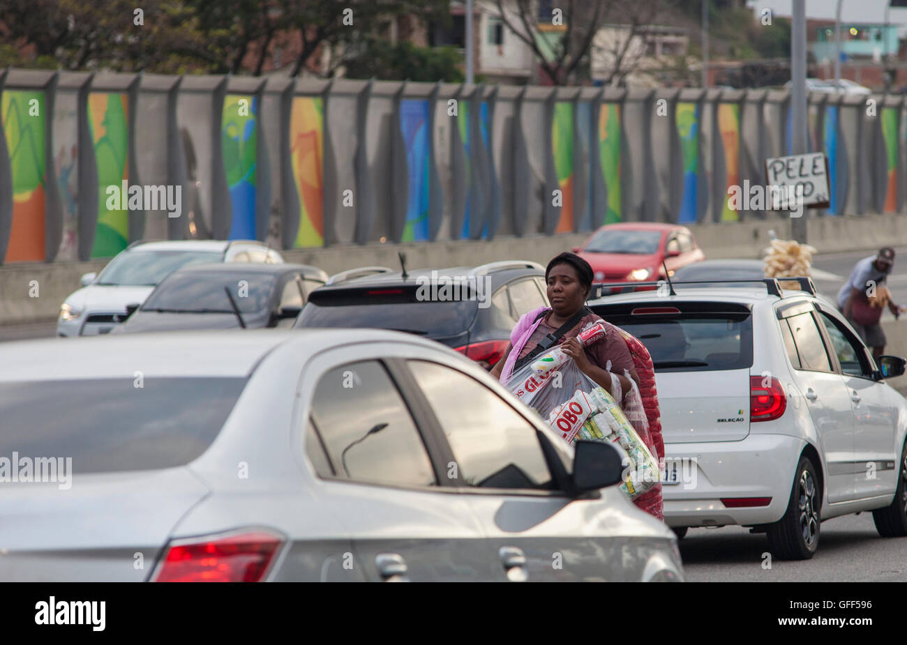 Habitants de Complexo da Mare, un immense réseau de favelas qui siège aux côtés de la Linha Vermelha ( ligne rouge ), la route principale de l'aéroport international de Rio de Janeiro au centre-ville, à travailler comme vendeurs de rue pendant les heures de pointe à l'expreessway - depuis 2010, la communauté a été clôturé à partir de l'autoroute par d'immenses panneaux Perspex - les autorités affirment qu'ils fournissent une barrière acoustique, les sections locales le décrivent comme un "mur de la honte", une autre façon de cacher les pauvres. Banque D'Images