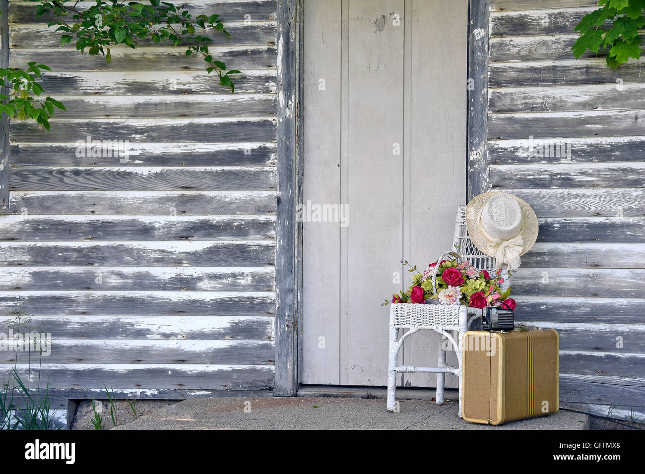 Vintage camera sur vieille valise par la porte en bois avec chapeau et fleurs à wicker chair. Banque D'Images