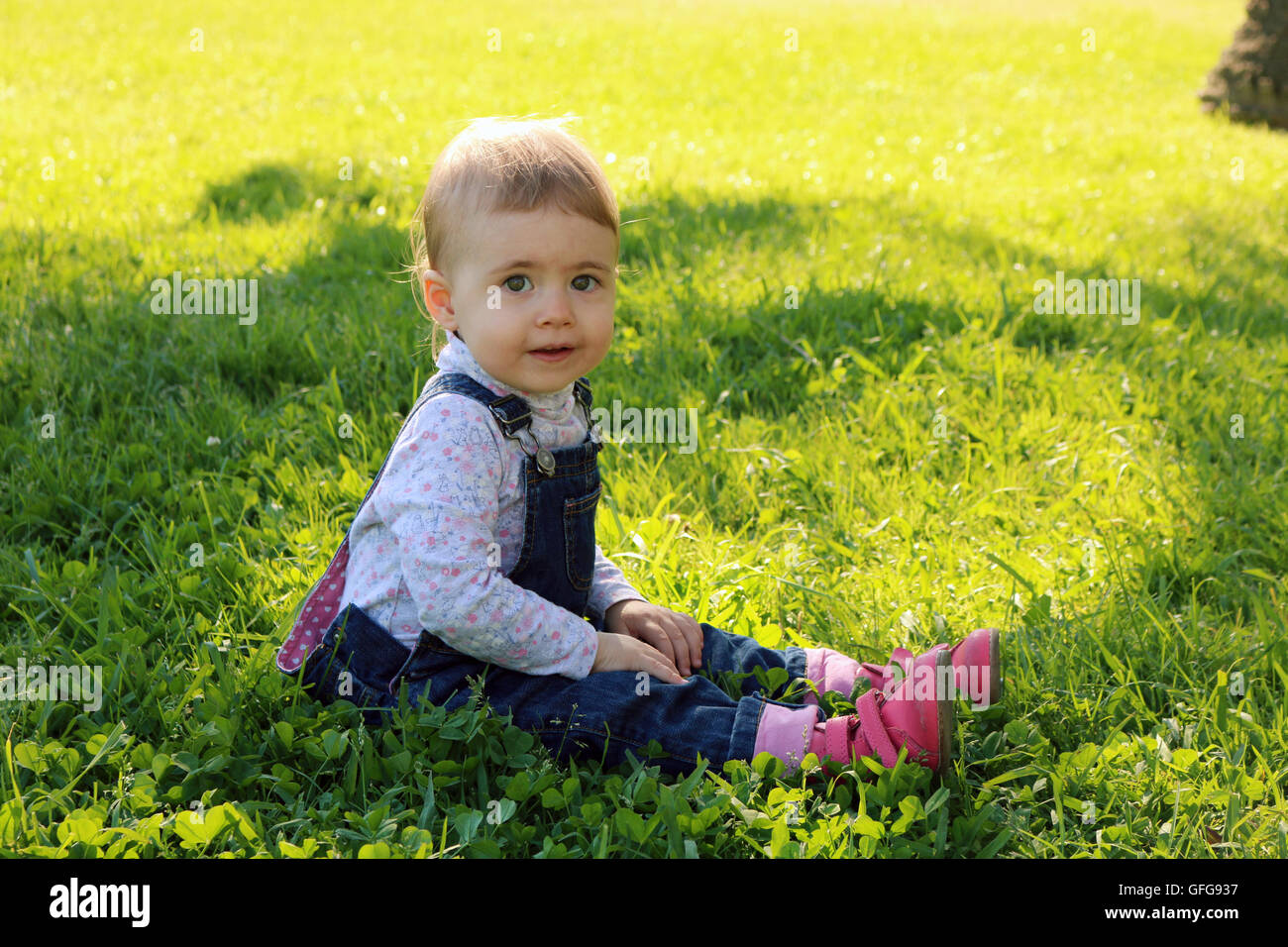 Lovely baby sitting sur l'herbe verte dans le parc et souriant pour l'été des jours heureux Banque D'Images