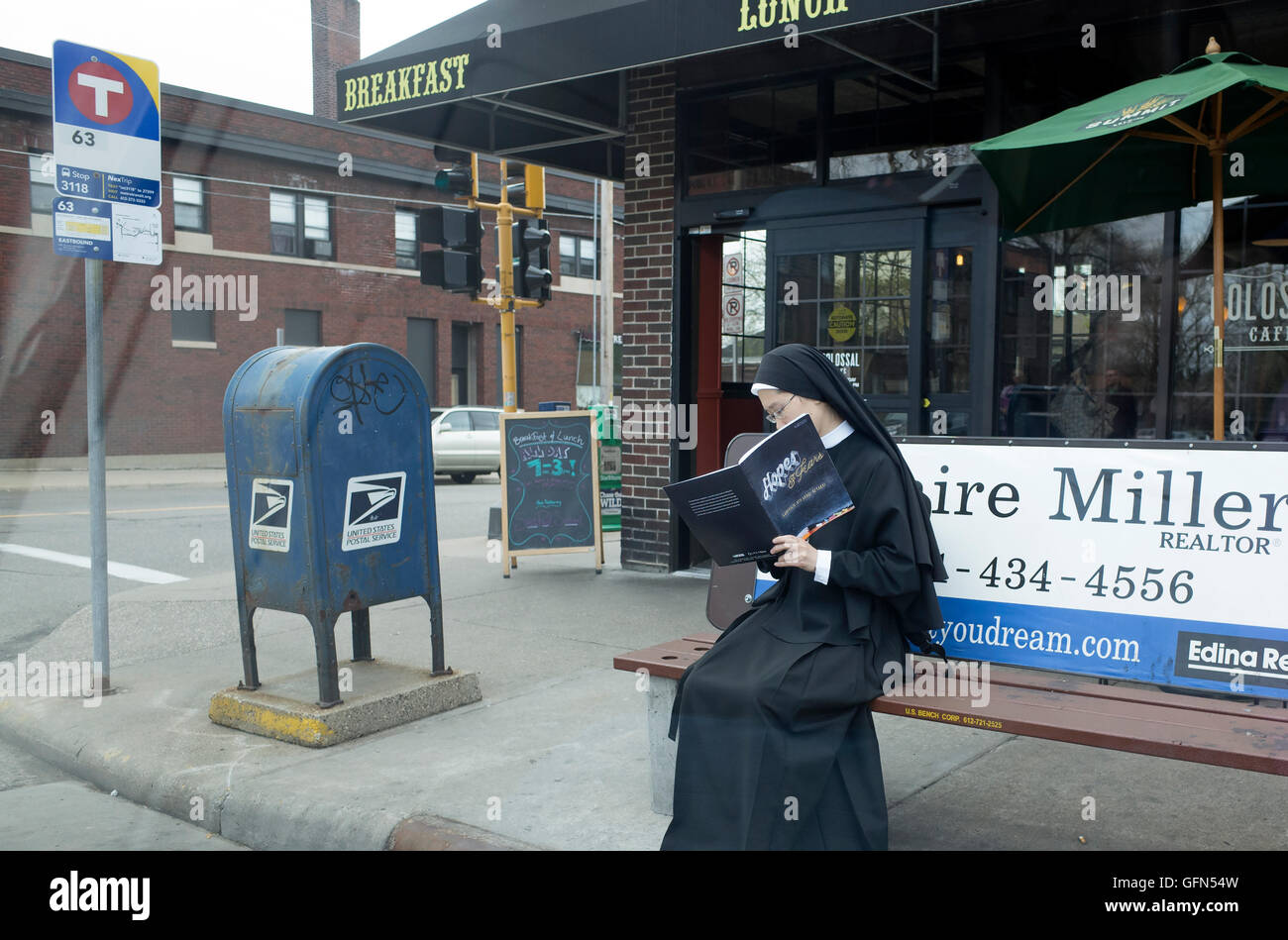 Nun de son habit assis sur un banc à l'arrêt de bus 4e année lecture brochure catholique espère et craintes. St Paul Minnesota MN USA Banque D'Images