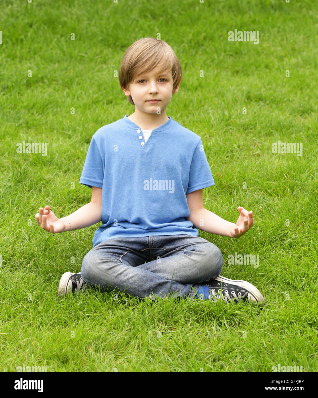 Cute blonde garçon assis sur l'herbe verte et méditer Banque D'Images
