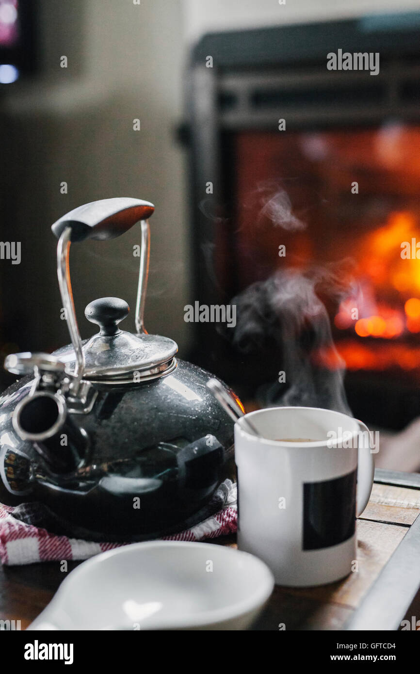 Un foyer d'accueil d'un feu allumé et une table avec un verre d'eau et café Banque D'Images