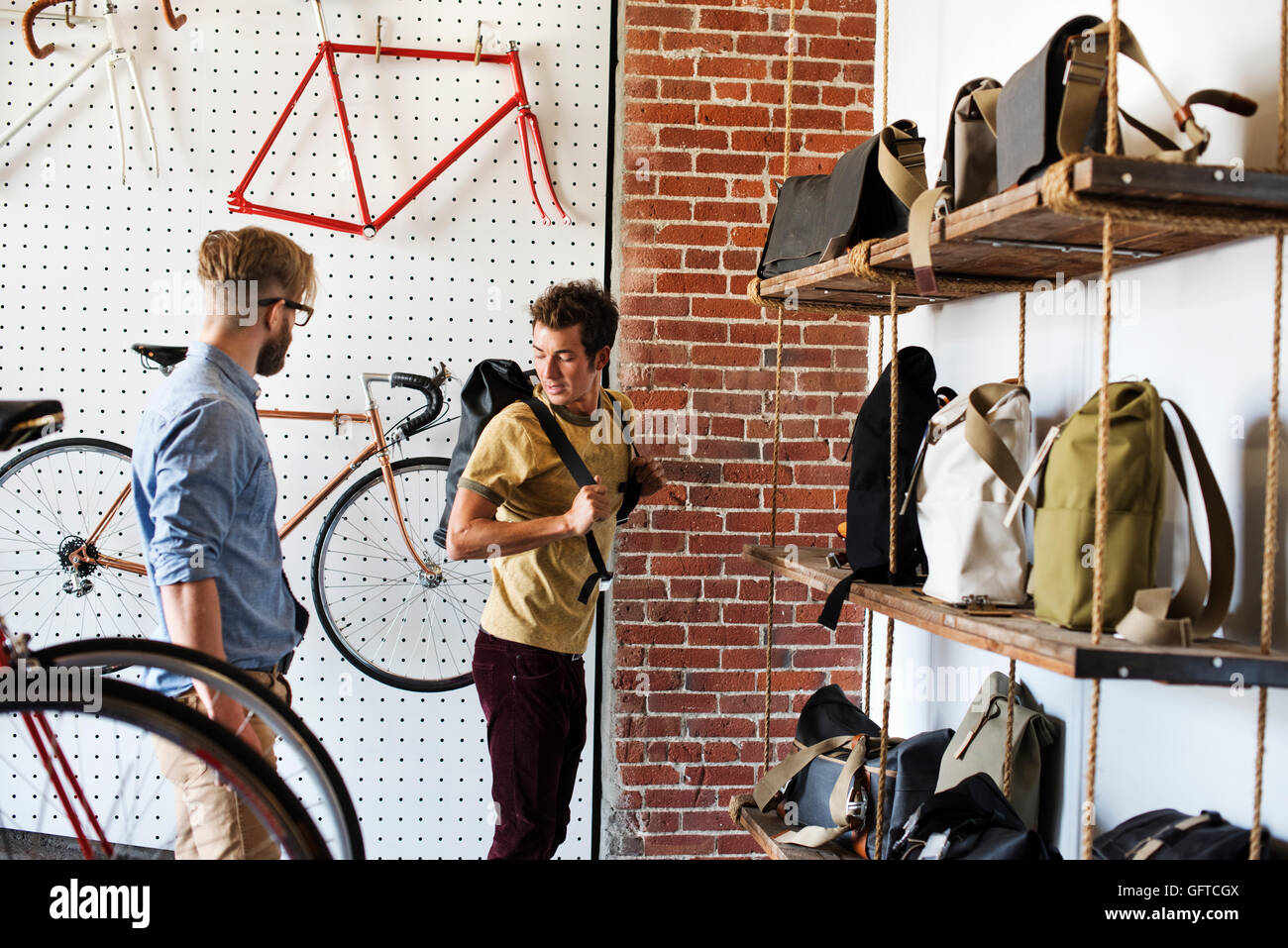 Deux hommes dans un atelier de réparation de vélo à un client à la recherche des sacs à dos et sacs de vélo Banque D'Images