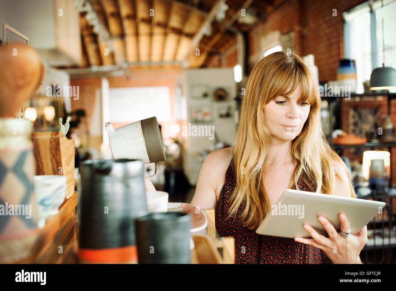 Femme dans un magasin tenant une tablette numérique et verseuse en céramique Banque D'Images