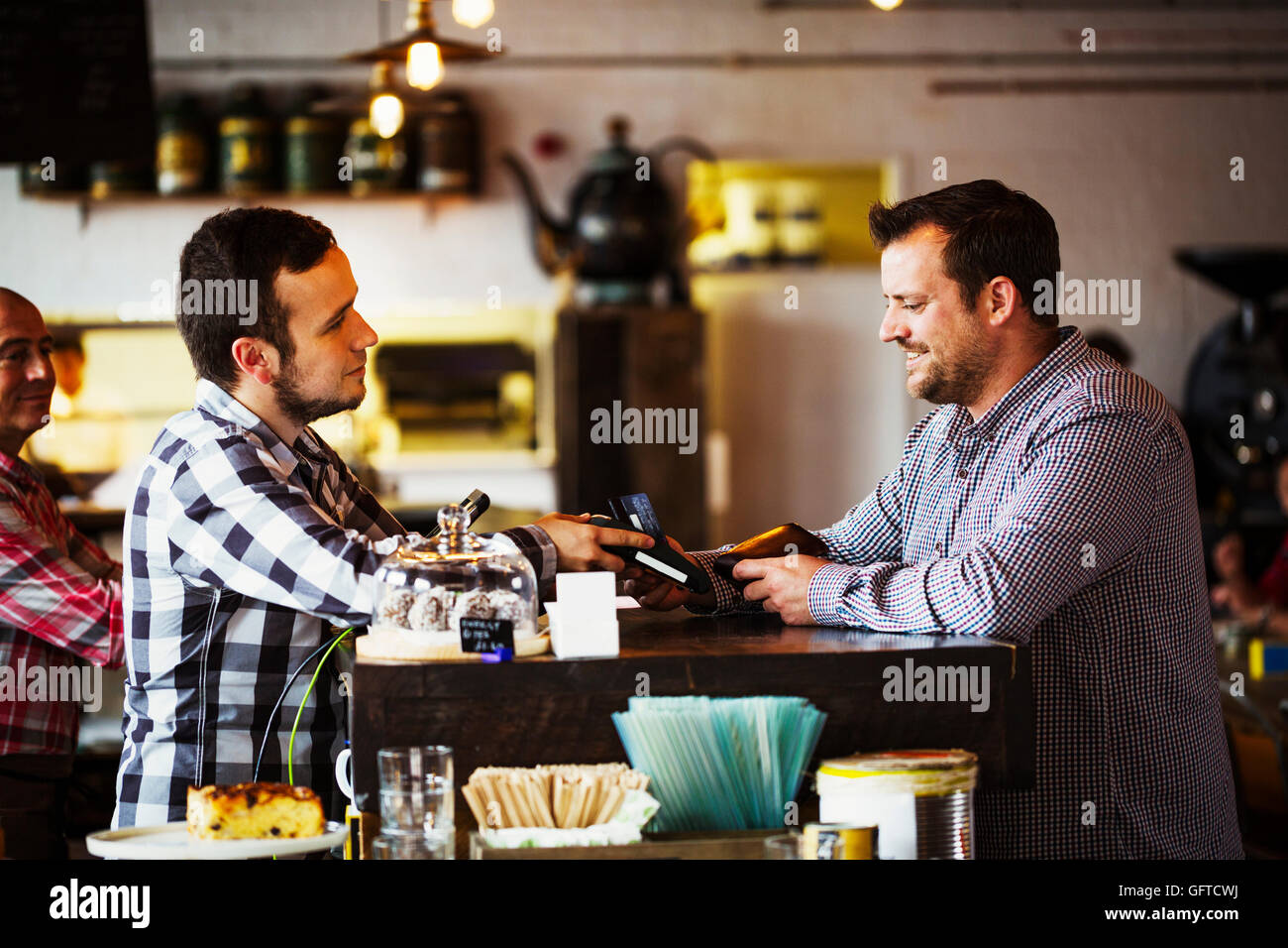 Deux hommes d'un barista et un client de conversations au comptoir du café Banque D'Images