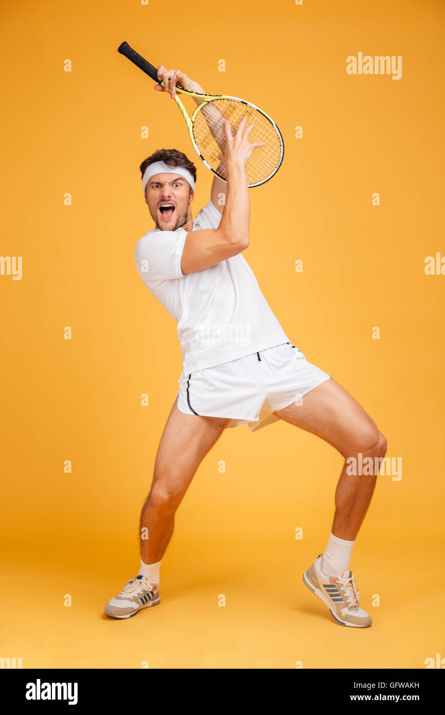 Jeune homme espiègle comique avec joueur de tennis racket en criant et en s'amusant sur fond jaune Banque D'Images