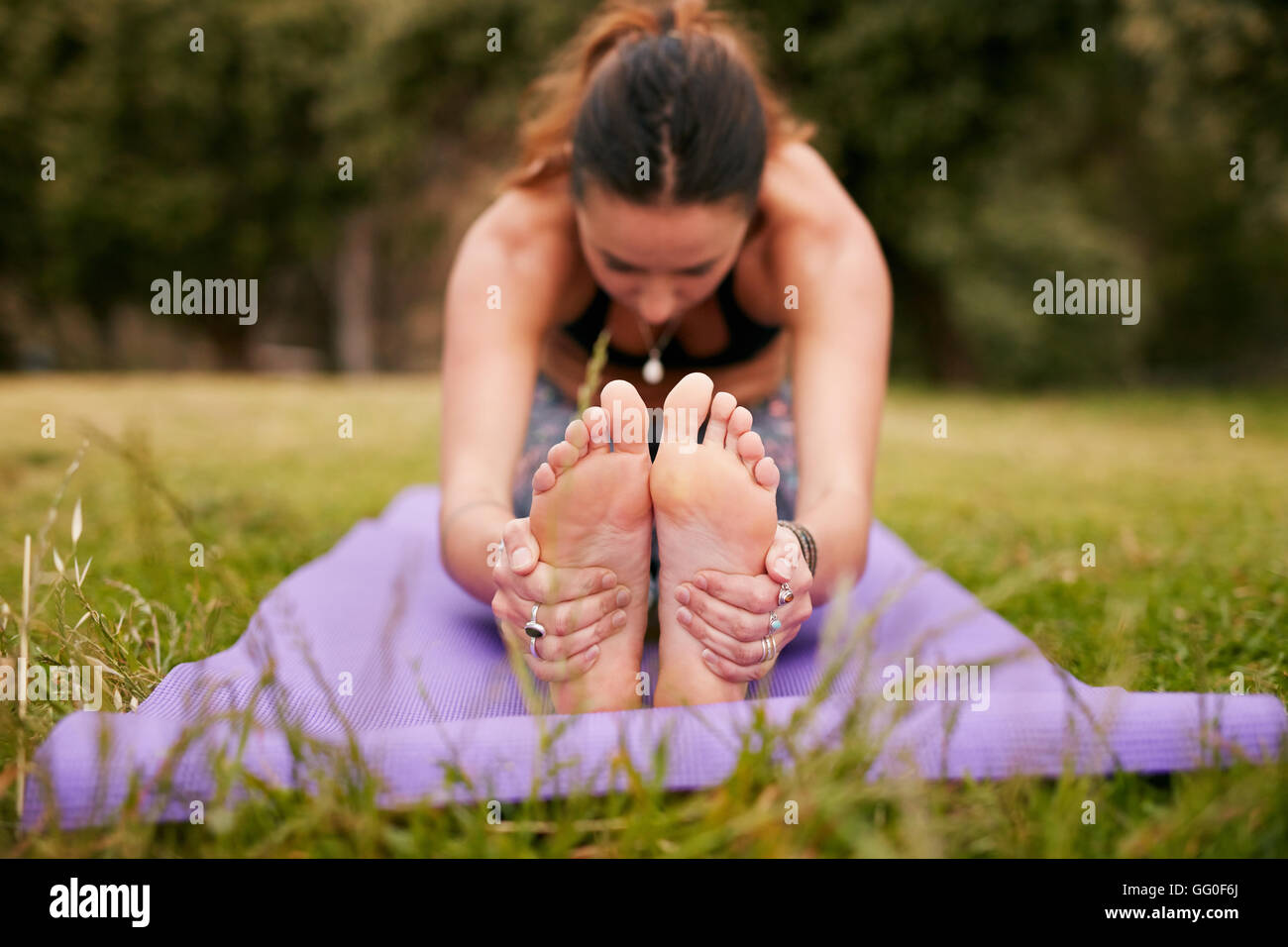 Woman sitting on exercise mat de fibres de l'avant et la tenue des pieds. Woman practicing yoga paschimottanasana en plein air sur l'herbe. Banque D'Images