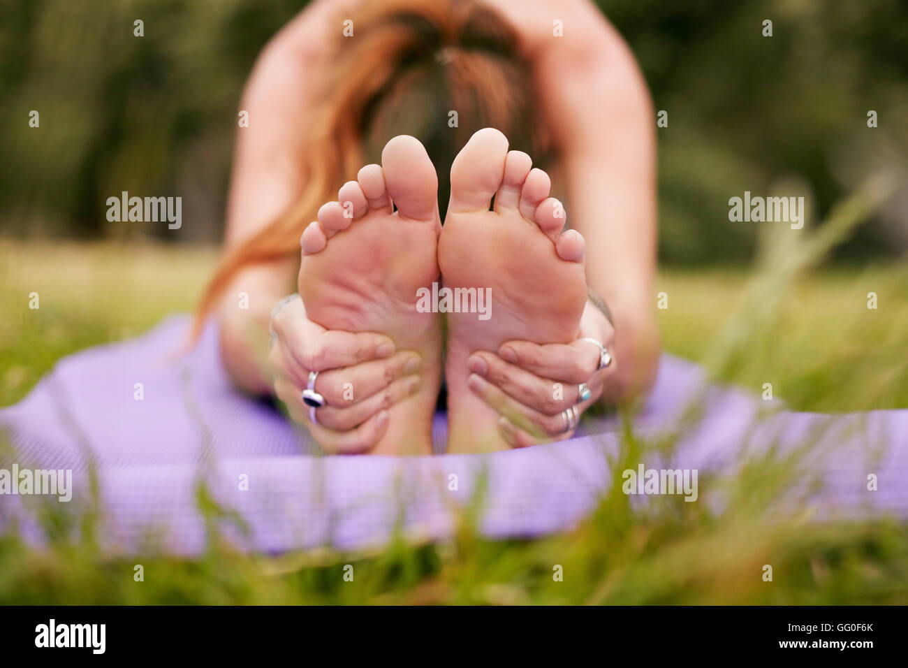 femme de fitness assise sur le tapis d'exercice se penchant vers l'avant et tenant les pieds. Femme pratiquant le yoga paschimottanasana sur l'herbe. Mise au point Banque D'Images