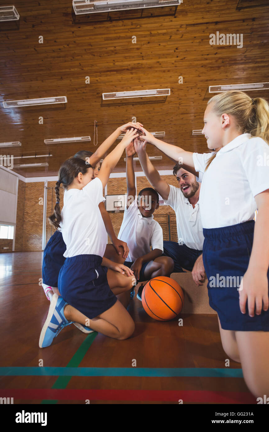 Professeur de sport et l'école les enfants formant part pile dans de basket-ball Banque D'Images