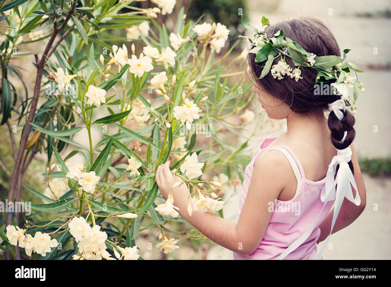 Une petite fille avec une couronne de fleurs admire les fleurs en fleurs, créant une scène sereine qui incarne la beauté et l'innocence de la nature dans un printemps doux Banque D'Images