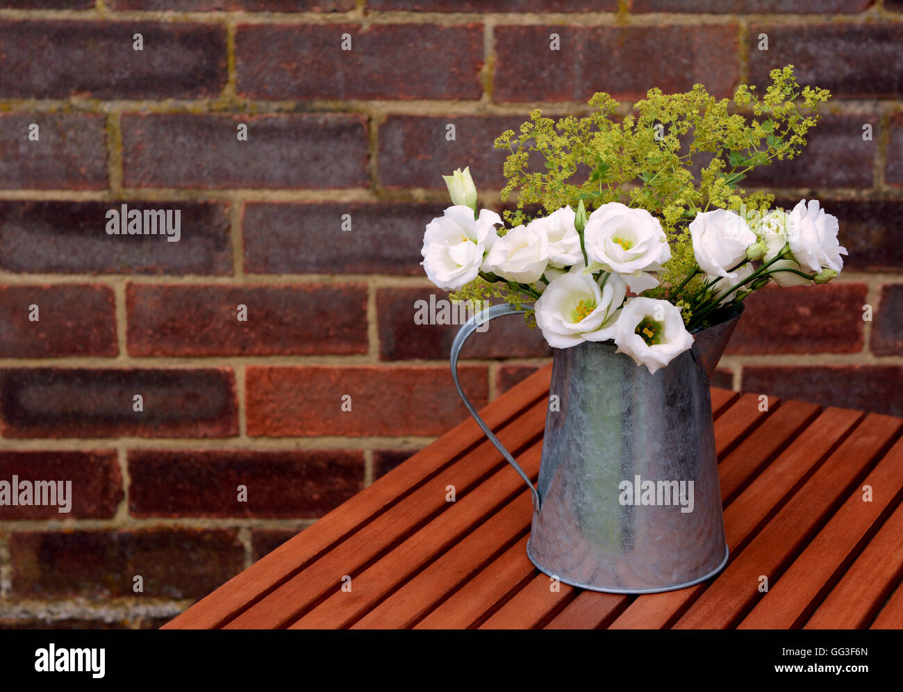 Gentiane blanche avec fleurs ladys dans un manteau metal cruche sur une table en bois contre un mur de brique avec copie espace Banque D'Images