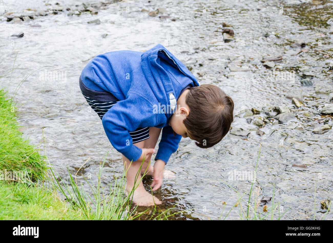 Un jeune garçon se lave les pieds dans un ruisseau Banque D'Images