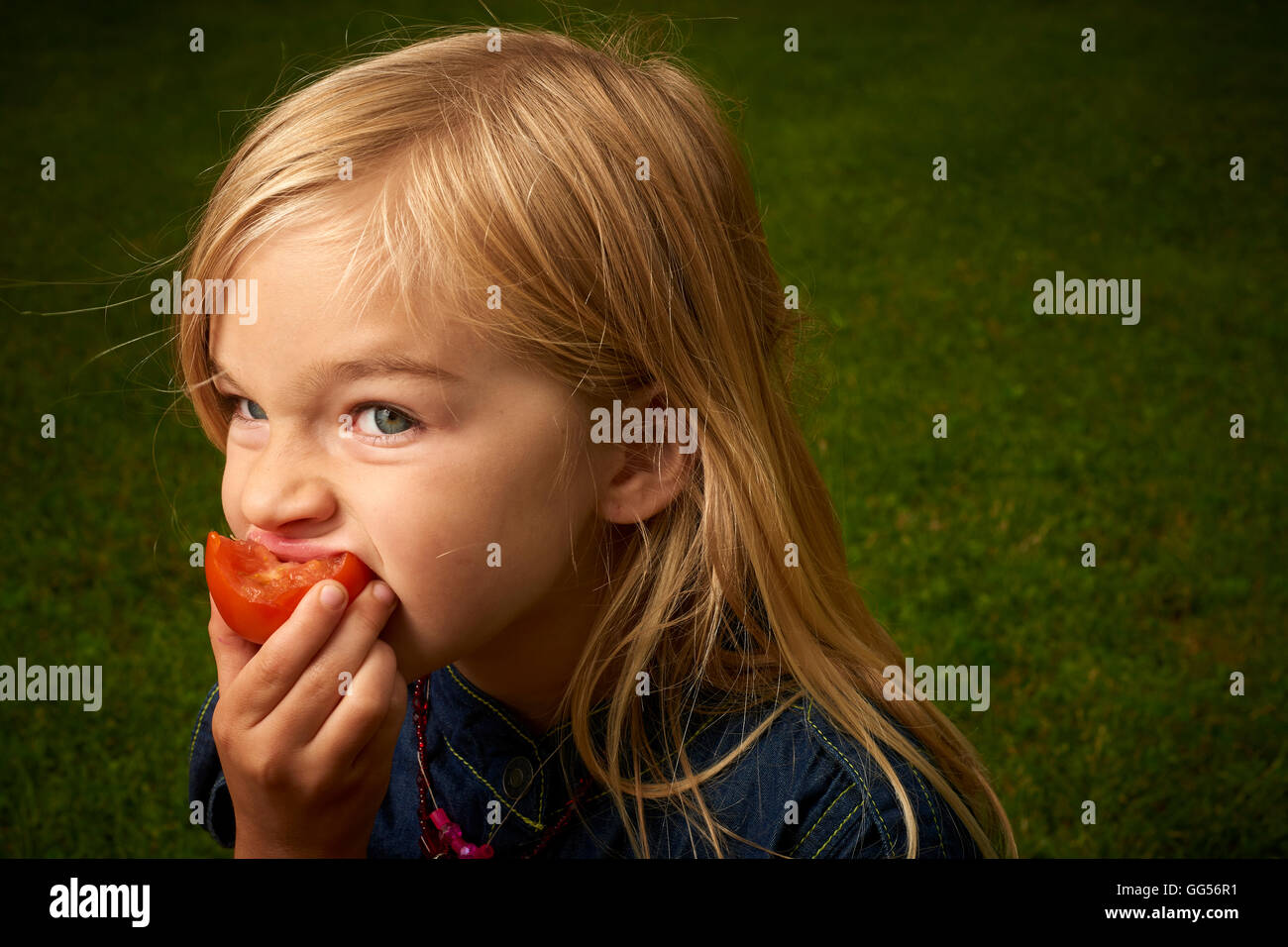 Cute blonde enfant girl eating tomato dehors dans le jardin Banque D'Images