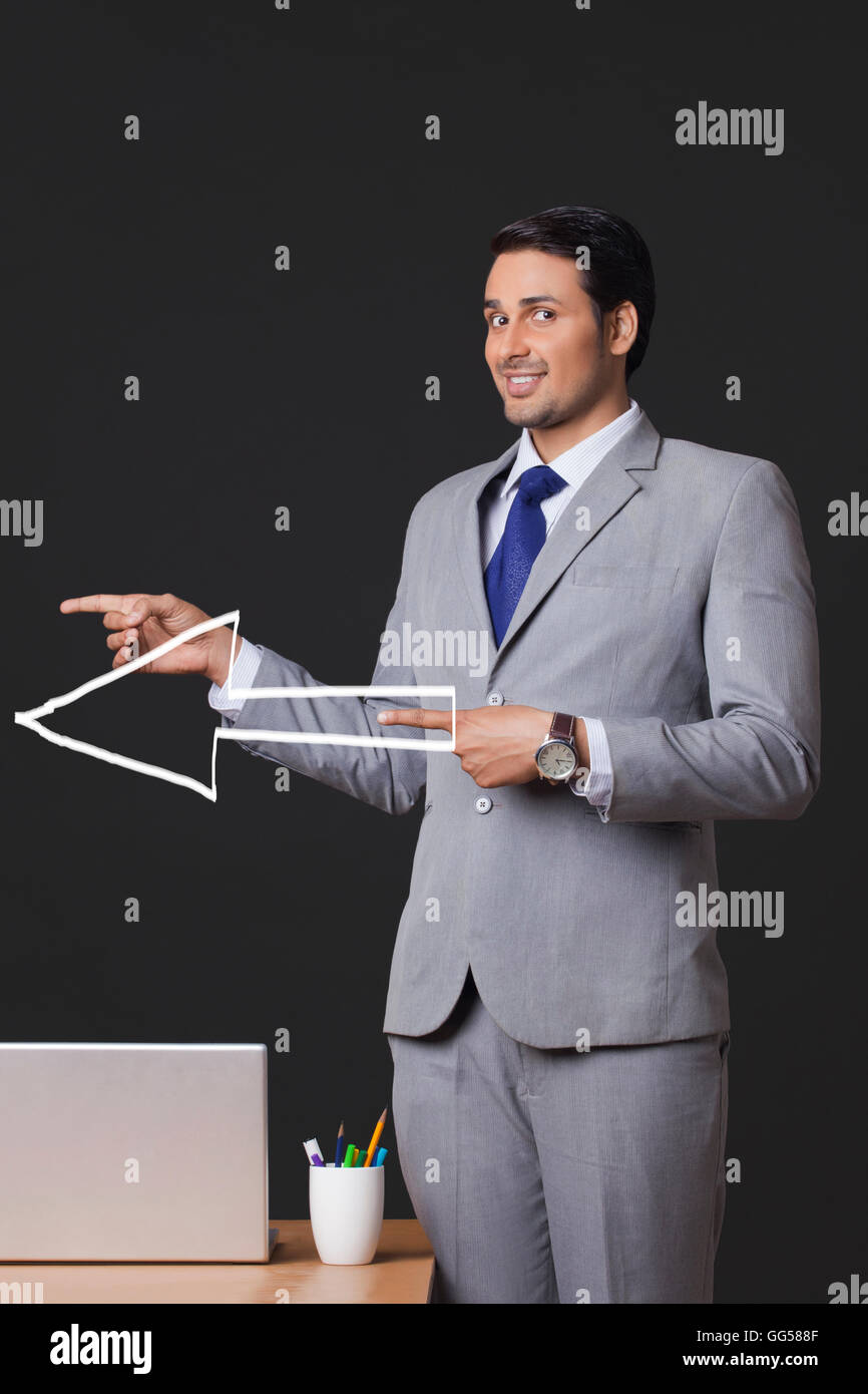 Portrait of young businessman avec panneau de flèche pointant latéralement dans office Banque D'Images