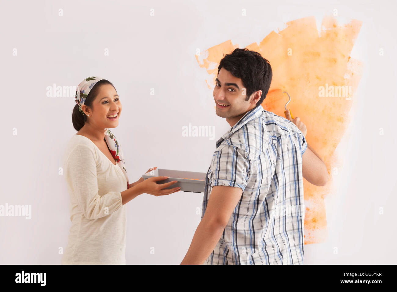 Beau jeune homme souriant de femme tout en appliquant de la peinture sur mur Banque D'Images