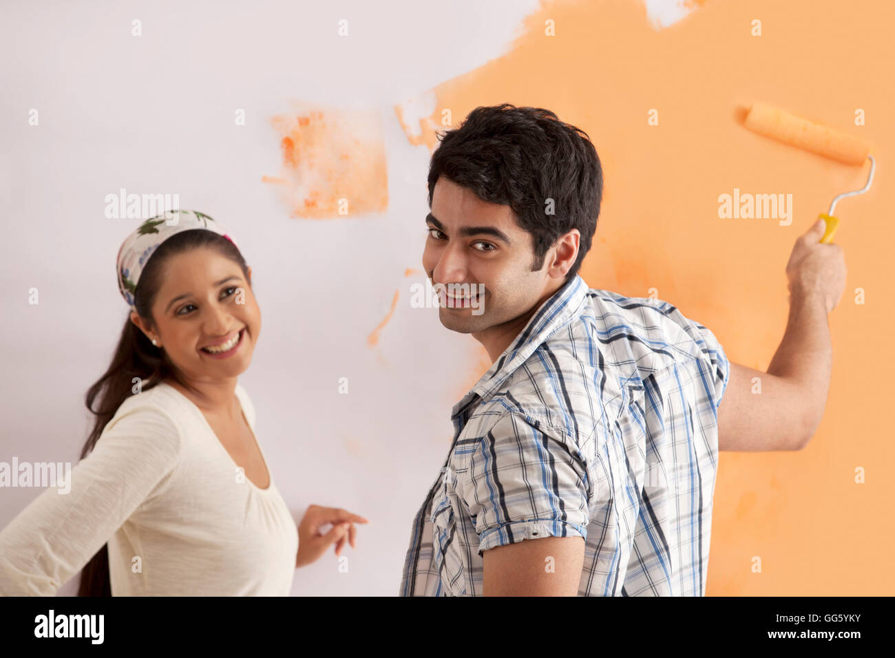 Portrait of smiling young man with woman l'application de peinture orange sur le mur Banque D'Images