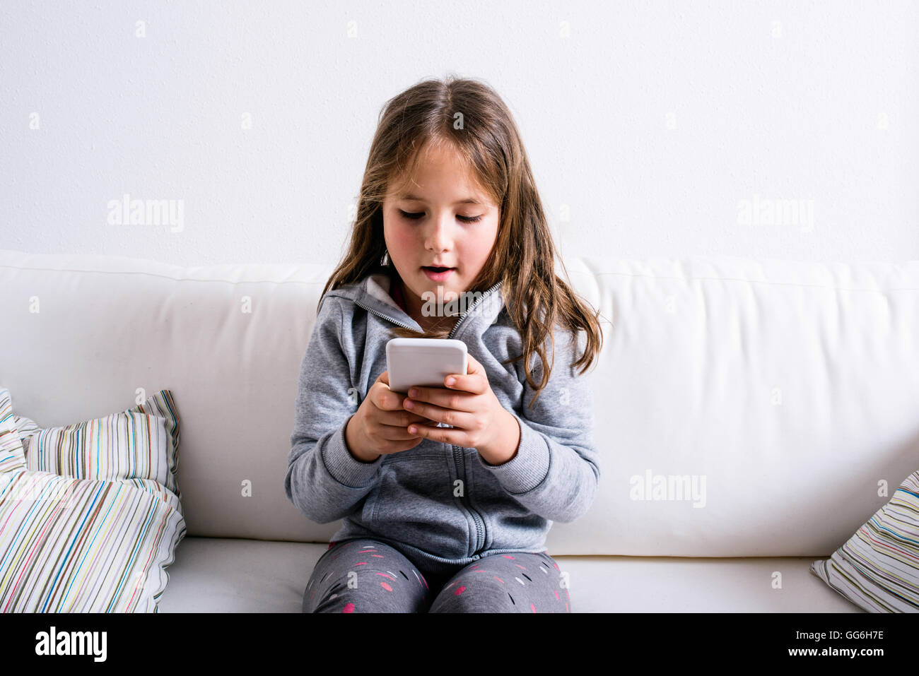 Petite fille assise sur le canapé, jouant avec le smartphone Banque D'Images