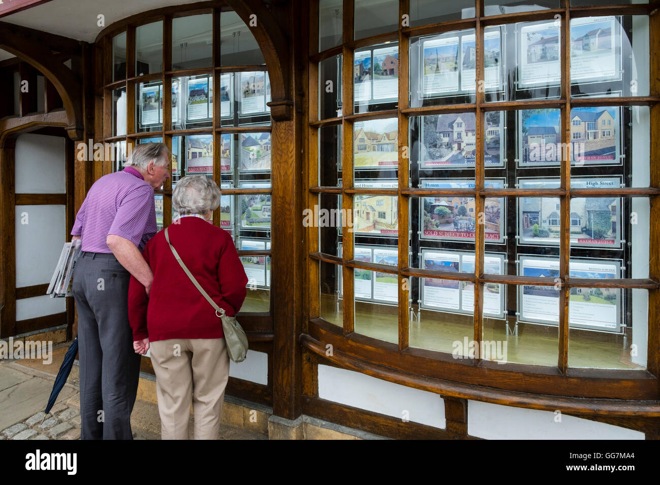 Couple dans les agents immobiliers à la fenêtre de propriétés en vente dans les Cotswolds en Angleterre, Royaume-Uni Banque D'Images
