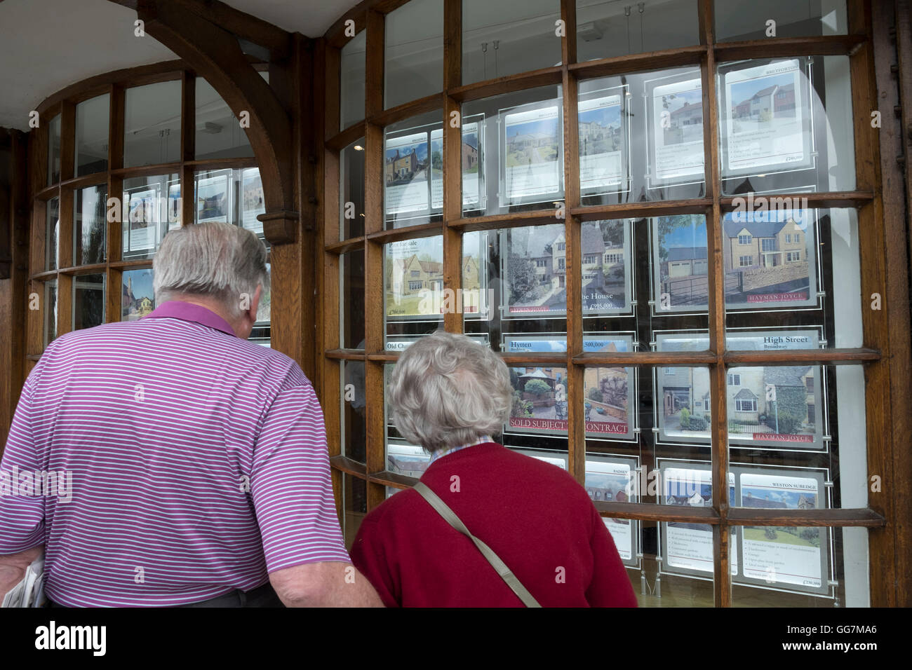 Couple dans les agents immobiliers à la fenêtre de propriétés en vente dans les Cotswolds en Angleterre, Royaume-Uni Banque D'Images