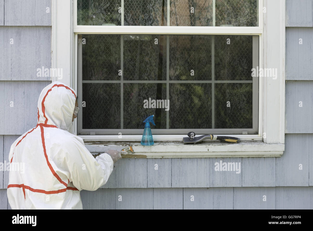 Un peintre dans une combinaison hazmat les éraflures de la peinture au plomb  dangereux hors d'un rebord de fenêtre Photo Stock - Alamy