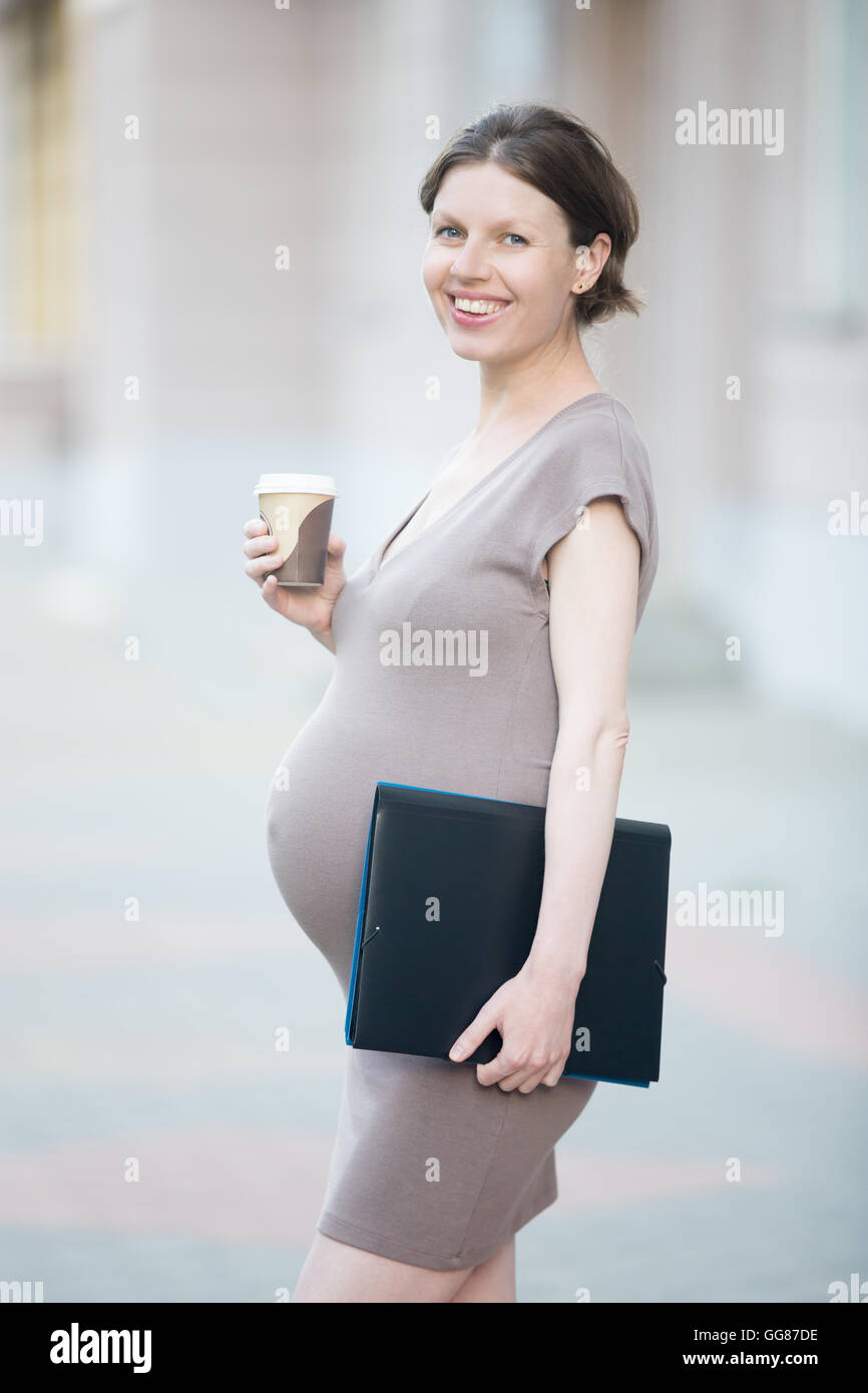 Maman active. Portrait of happy young pregnant woman looking at camera en étant debout sur la rue avec dossier de document Banque D'Images