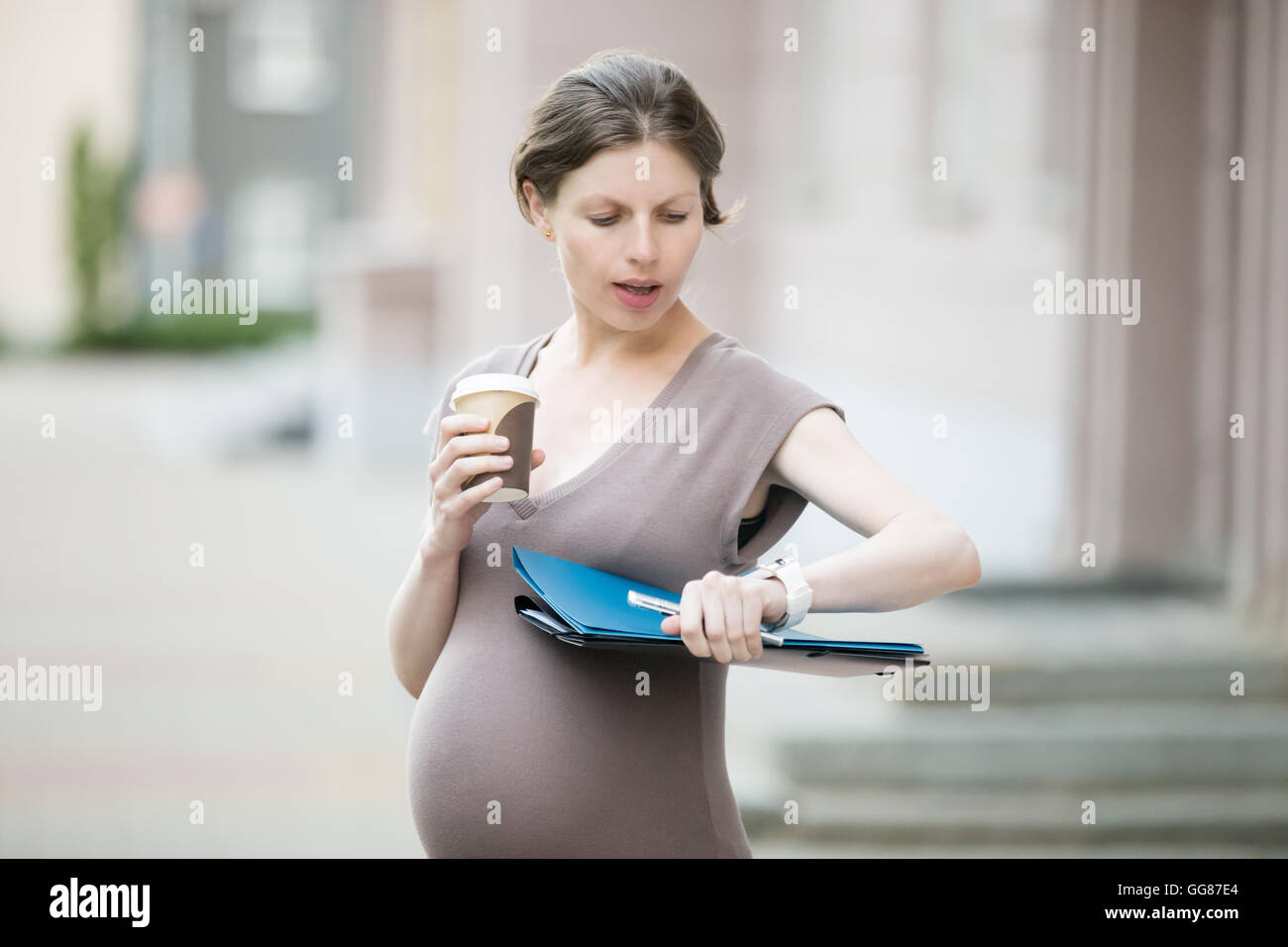 Portrait of young pregnant woman with business dossier document looking at watch. Office worker femme enceinte se dépêcher, en attente Banque D'Images