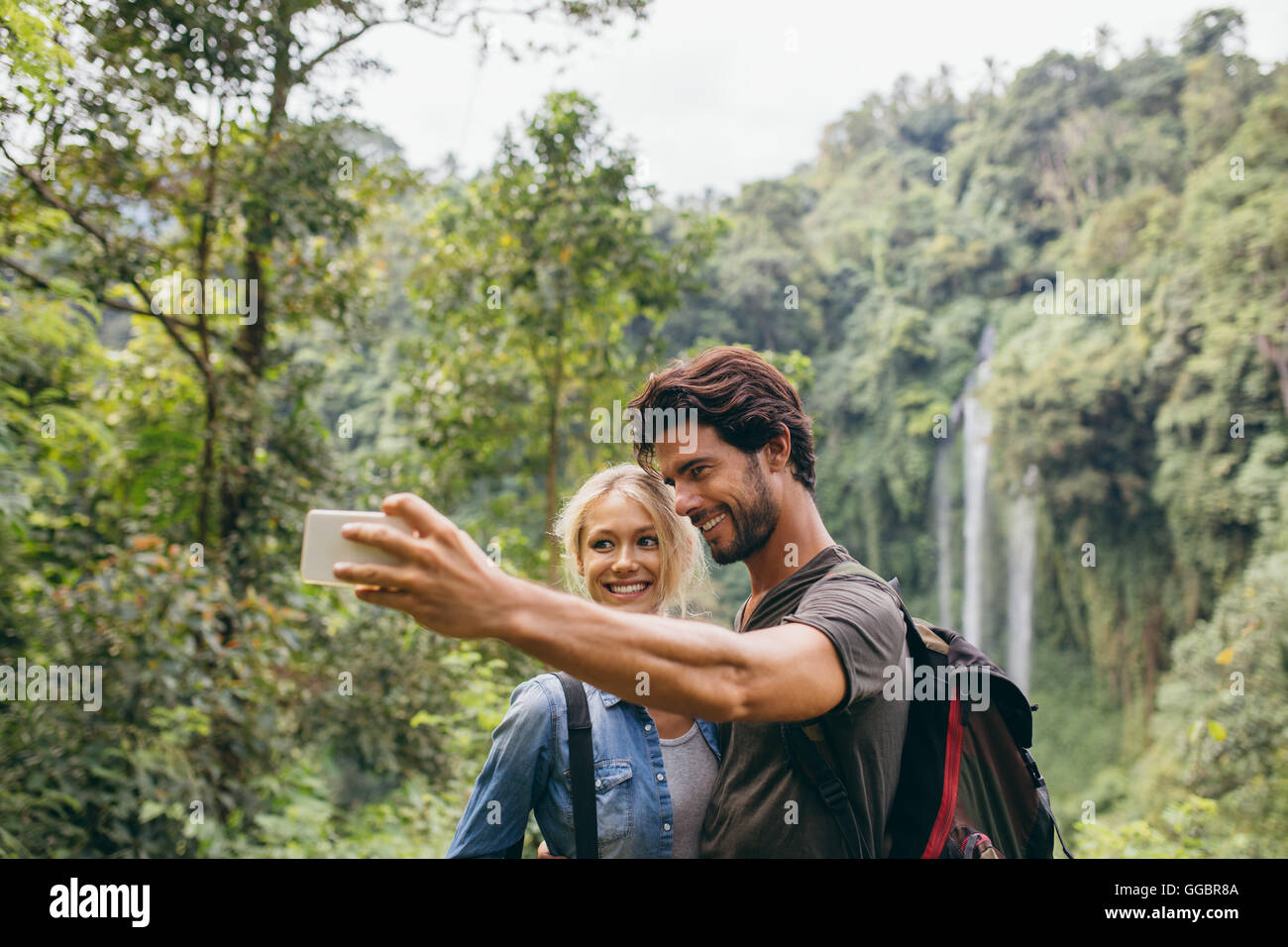 Happy young couple taking self portrait avec leur téléphone cellulaire sur journée de randonnée. Couple taking photo en face d'une cascade. Banque D'Images