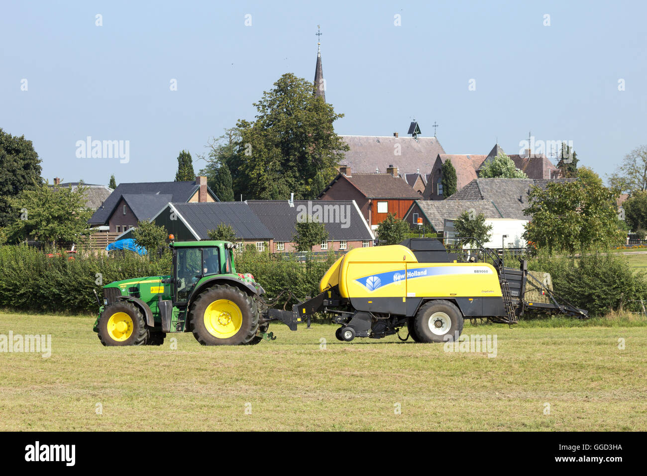Avec un tracteur John Deere Ramasseuse-presse New Holland Banque D'Images