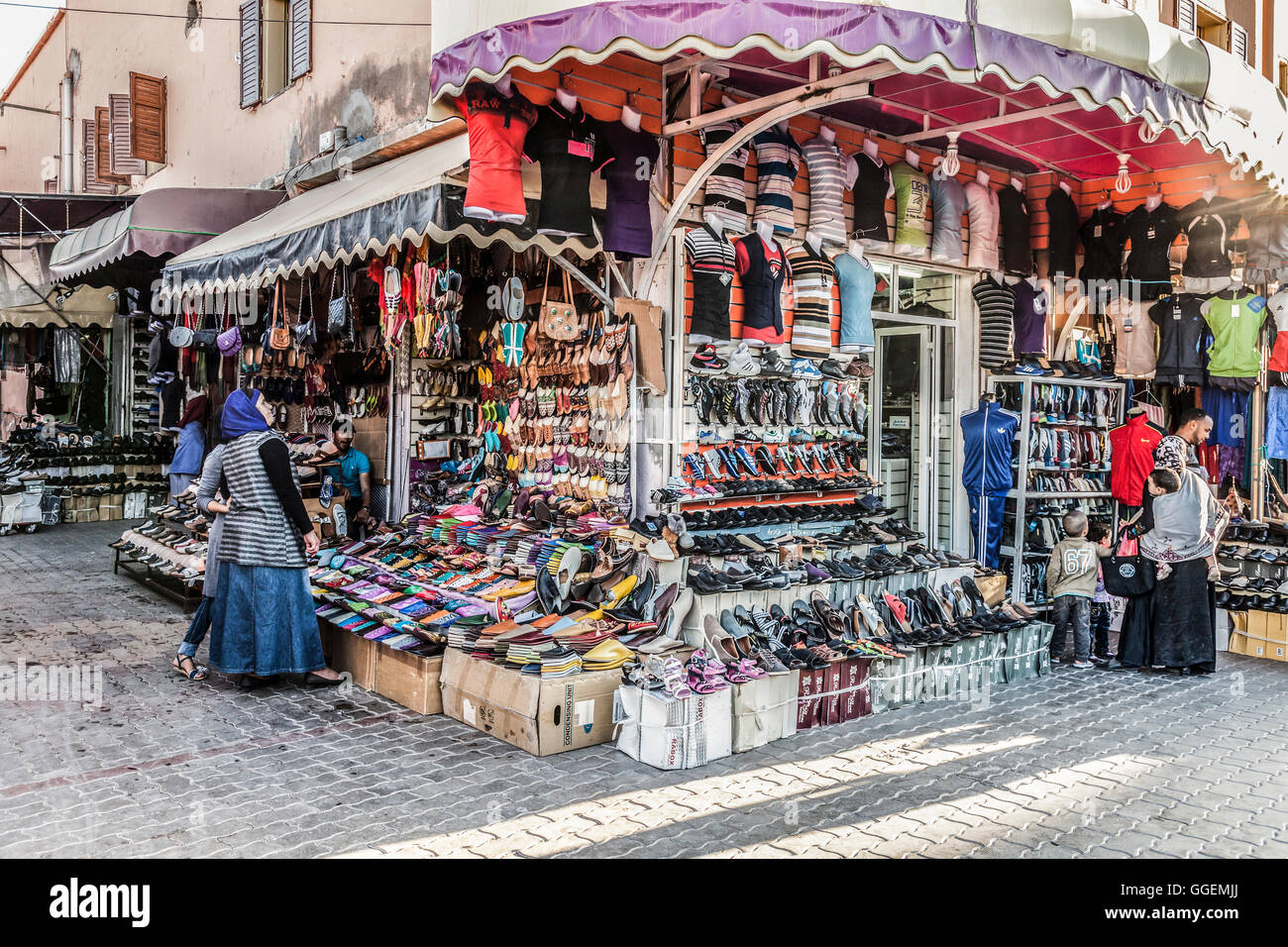 Fournisseurs et consommateurs dans un groupe d'étals de vente chaussures, sacs et vêtements de sport dans une rue au centre-ville de Ouarzazate, Maroc. Banque D'Images
