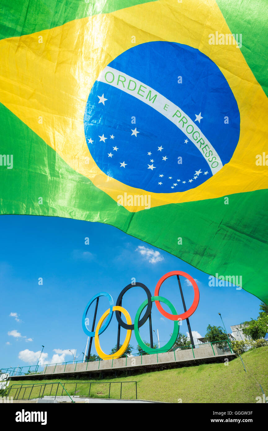 RIO DE JANEIRO - le 18 mars 2016 : un drapeau du Brésil s'arrête en face de l'affichage des anneaux olympiques dans la région de Parque Madureira Park. Banque D'Images
