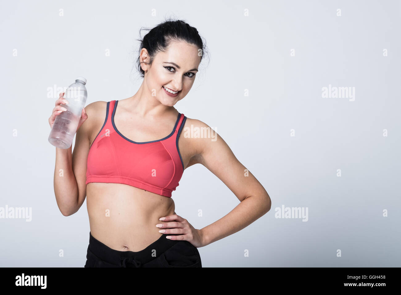 Femme dans la vingtaine dans l'équipement de fitness tenant une bouteille d'eau dans un studio sur un fond blanc. Il y a un espace de copie à droite de l'image Banque D'Images