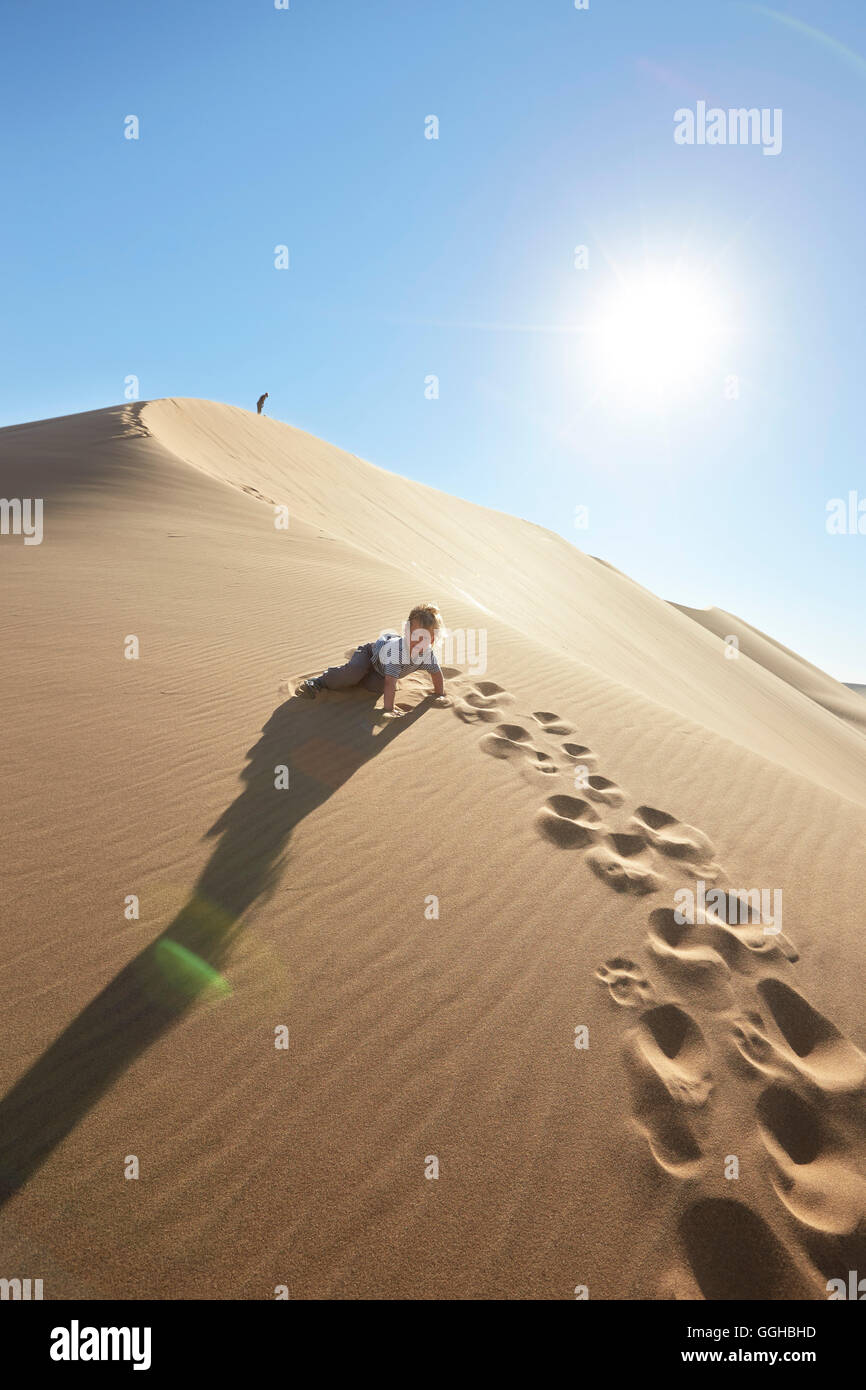 Boy crawling up une dune de sable, Dune 7, Walvis Bay, Erongo, Namibie Banque D'Images