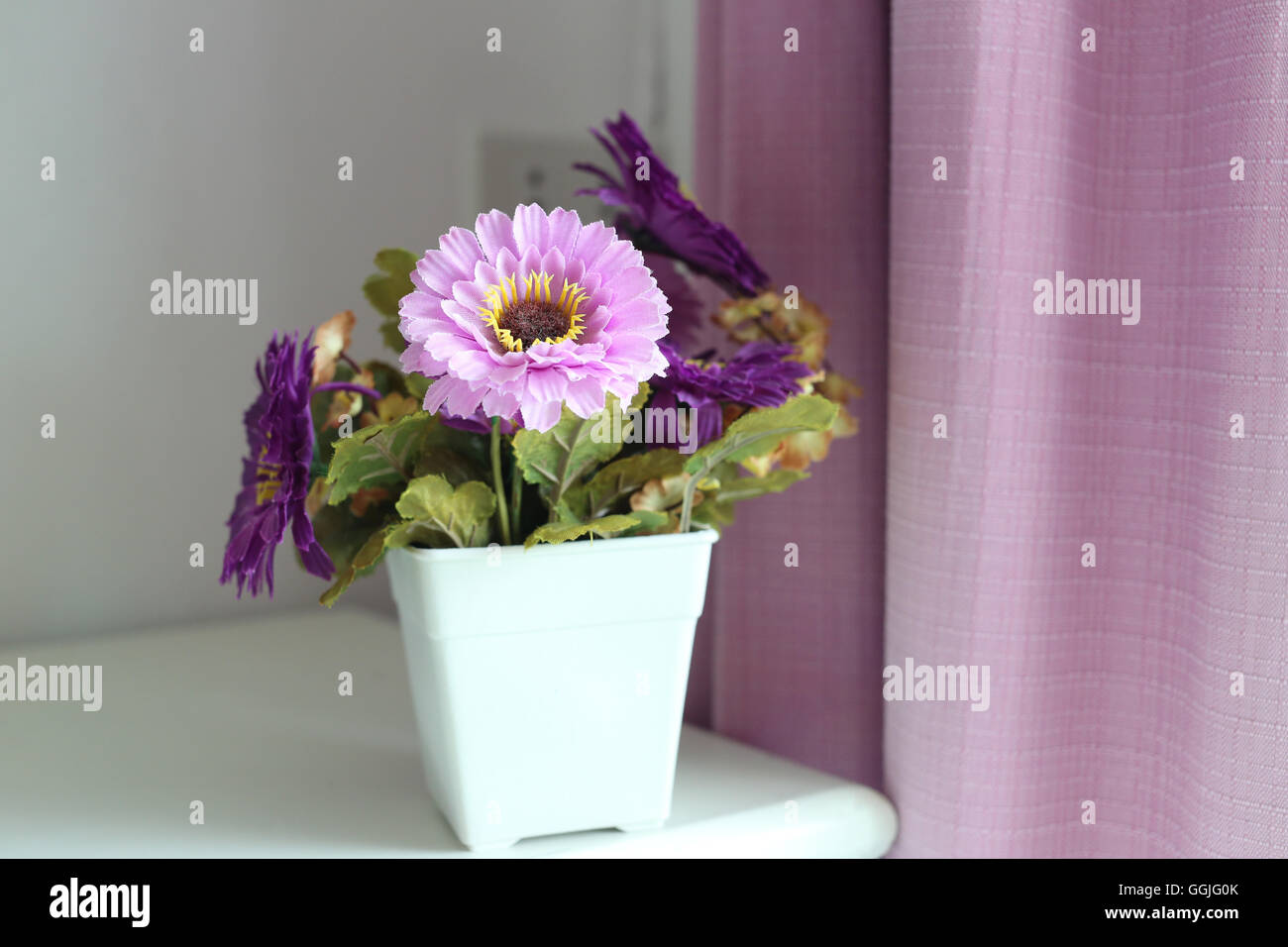 Fleurs violettes artificiel dans un vase blanc placé à côté de la fenêtre dans la chambre à coucher. Banque D'Images