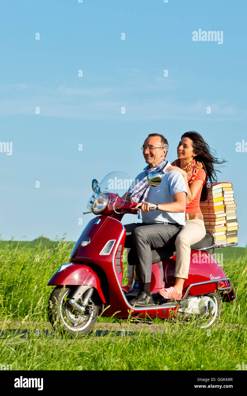 Un homme et une femme transportant une pile de livres sur un scooter Vespa rouge, Bad Wildungen, Hesse, Germany, Europe Banque D'Images