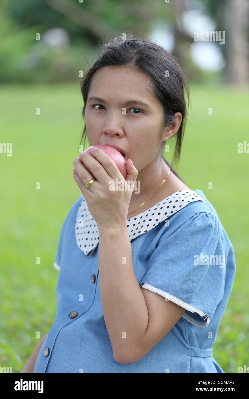 Les femmes enceintes asiatiques à l'aide de prises de main en mangeant apple dans le parc public. Banque D'Images