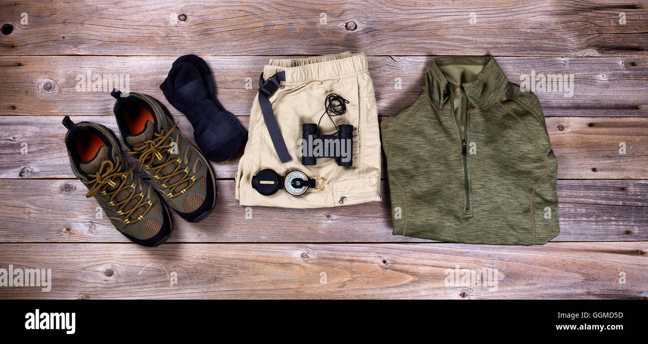 Vue de dessus d'équipement de randonnée : chaussures de randonnée, short, chemise, boussole, des chaussettes et des jumelles sur les planches de bois rustique Banque D'Images