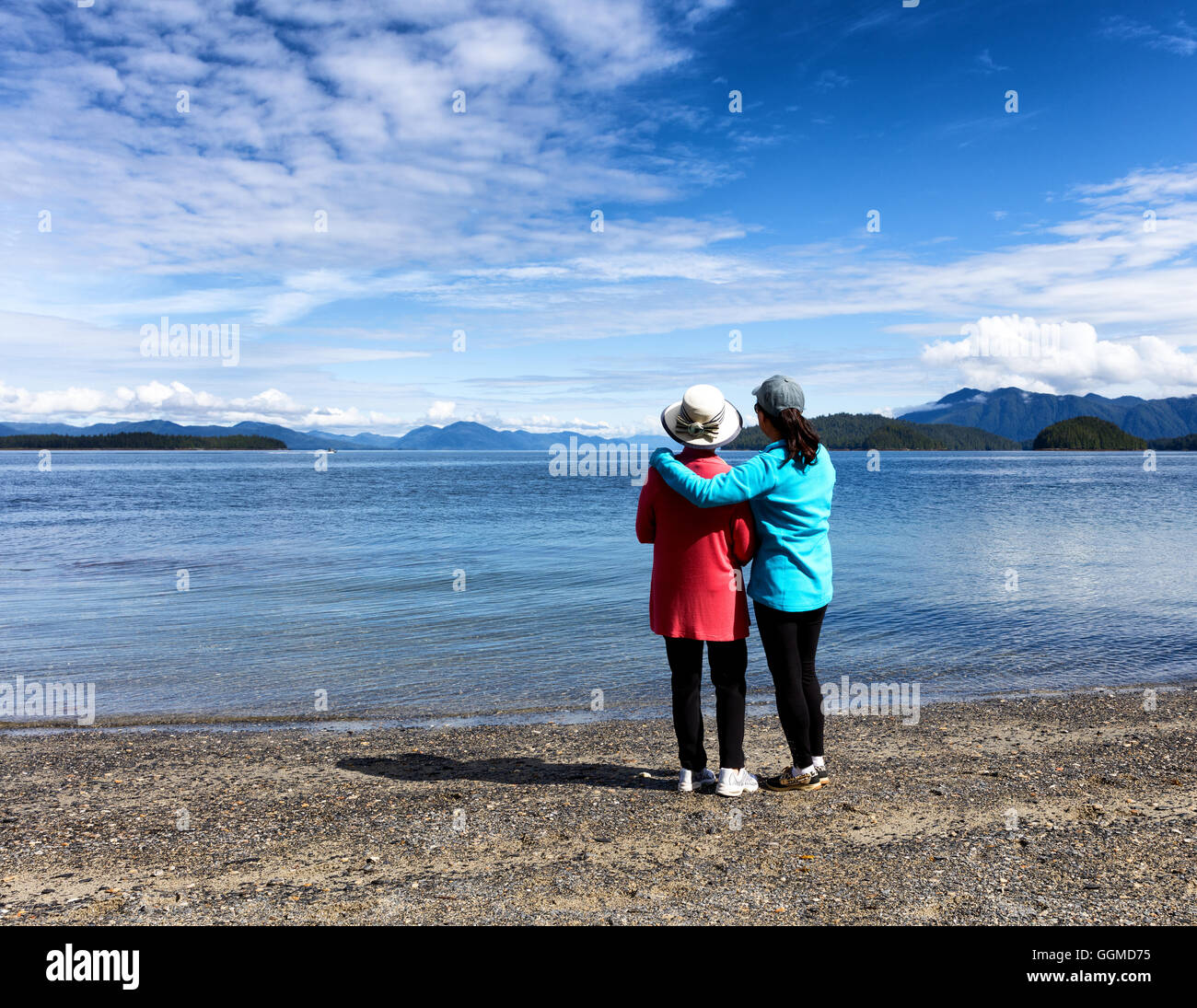 Mère et fille, à l'opposé de l'appareil photo, profiter du plein air sur un beau lac avec des montagnes et le ciel en arrière-plan. Banque D'Images