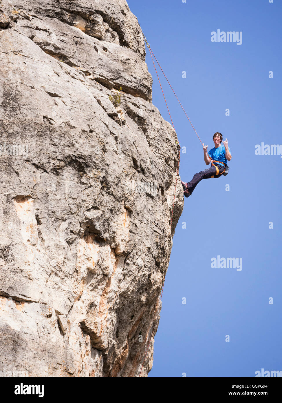 Caucasian man climbing rock gesticulant avec langue Banque D'Images