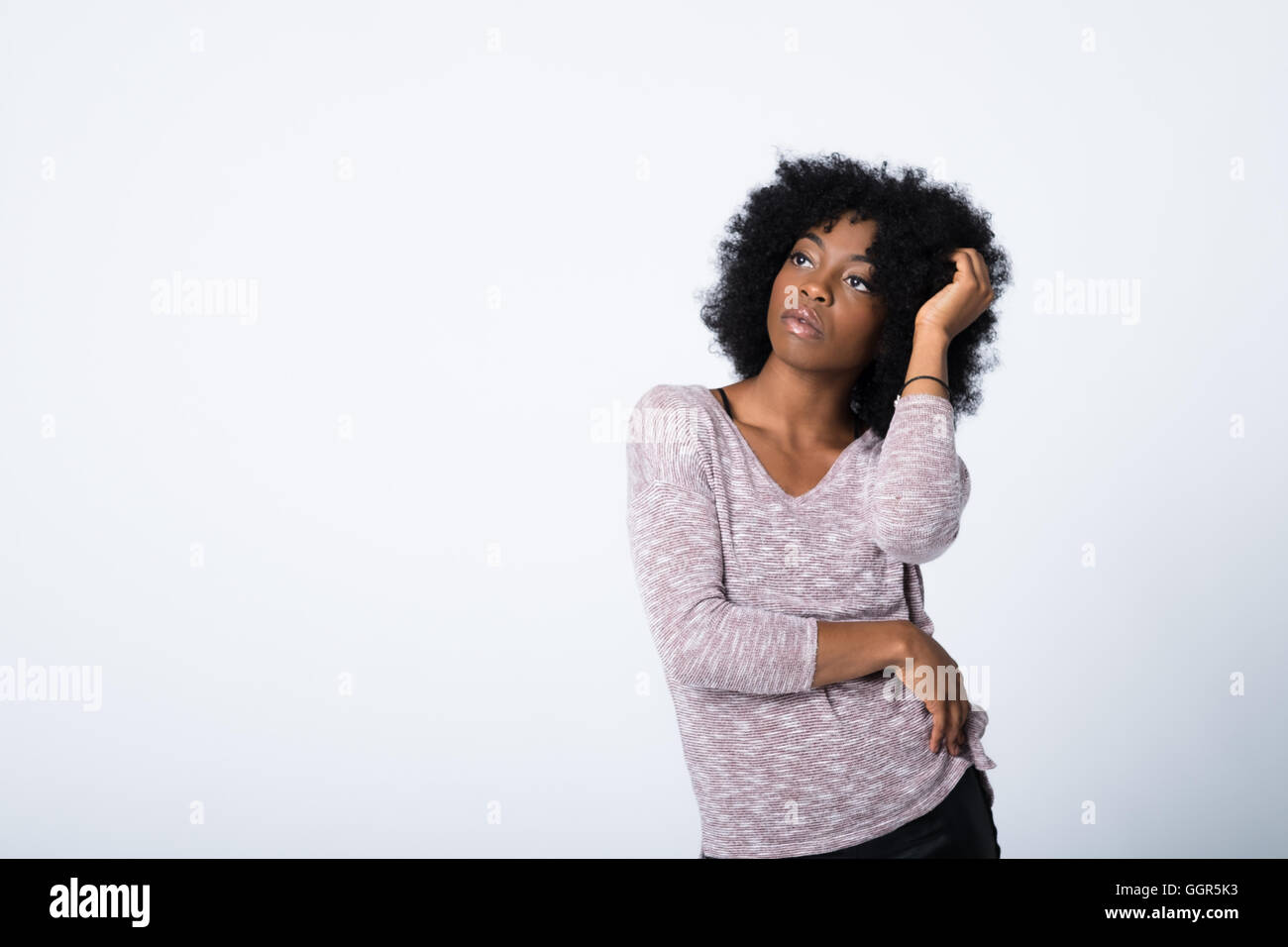 Image de mode d'une jeune femme afro-caribéenne dans sa vingtaine regardant en haut à gauche du cadre avecune main dans ses cheveux laissant l'espace de copie à gauche Banque D'Images