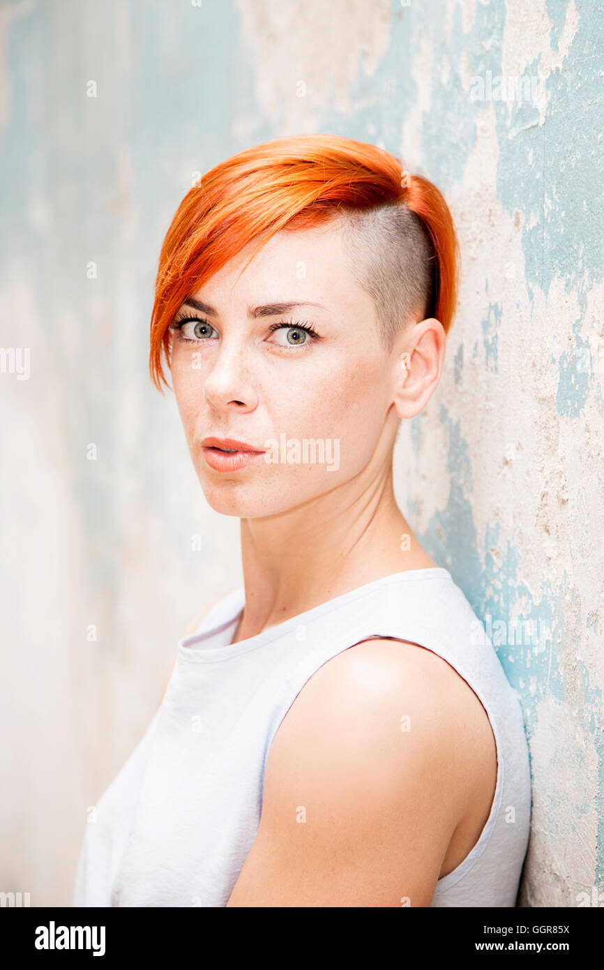 Jeune femme cheveux rouge moderne avec côté hairstlye rasée par le vieux mur permanent Banque D'Images