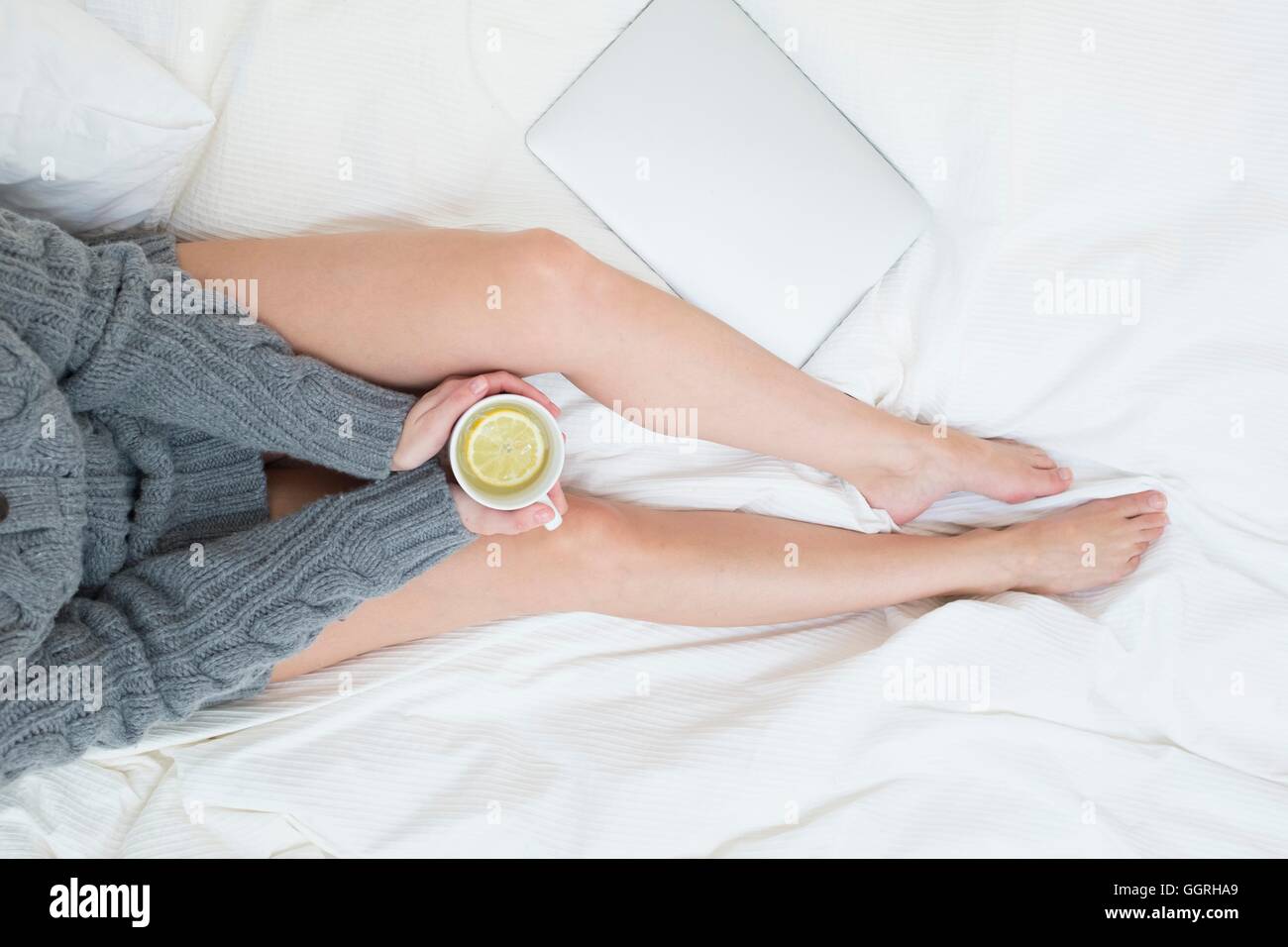 Femme assise sur le lit avec une tasse de boisson citron chaud. Banque D'Images
