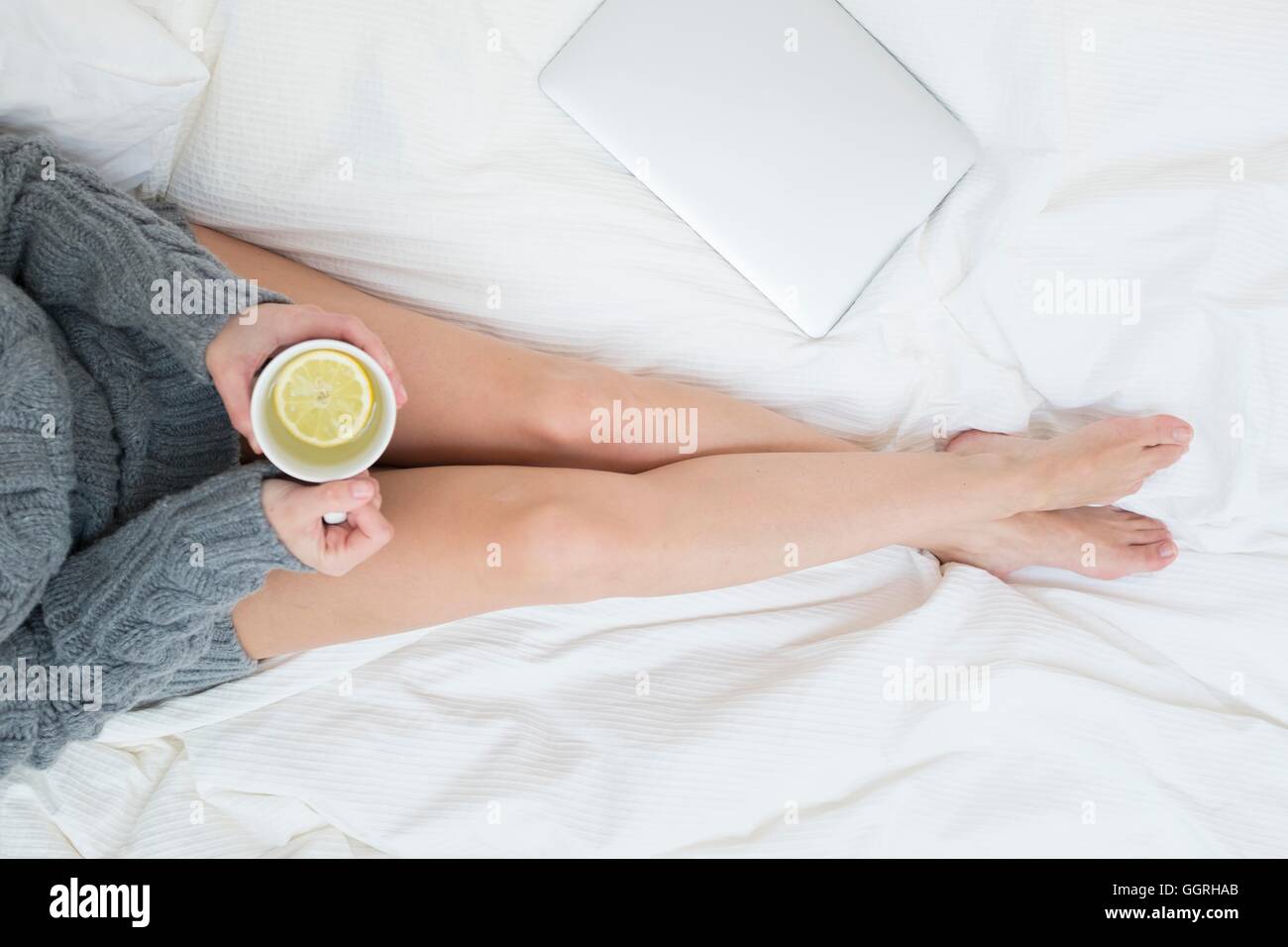 Femme assise sur le lit avec une tasse de boisson citron chaud. Banque D'Images