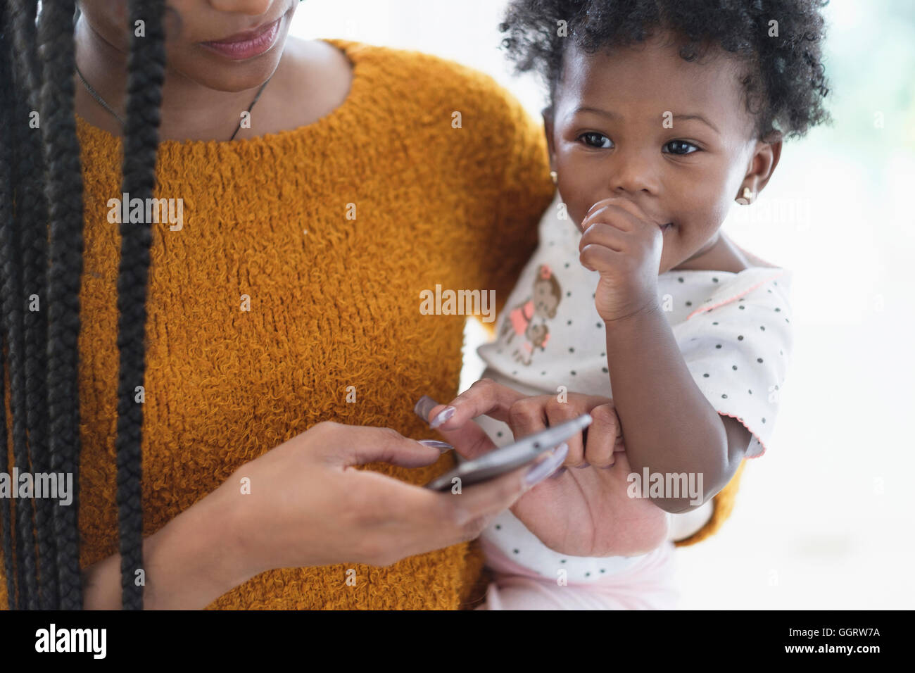 Black woman holding baby daughter using cell phone Banque D'Images